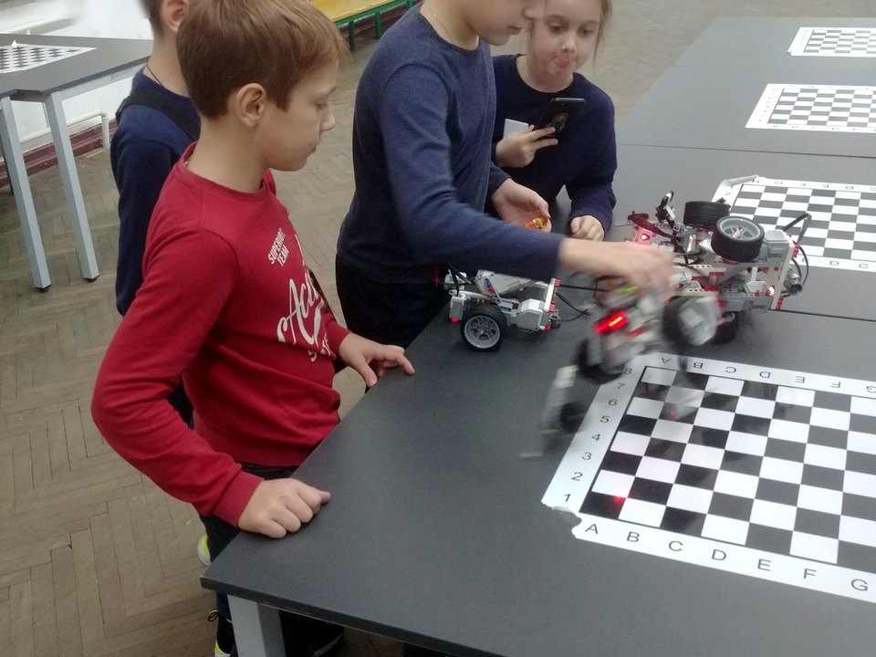 Children testing small wheeled robots on a tabletop.
